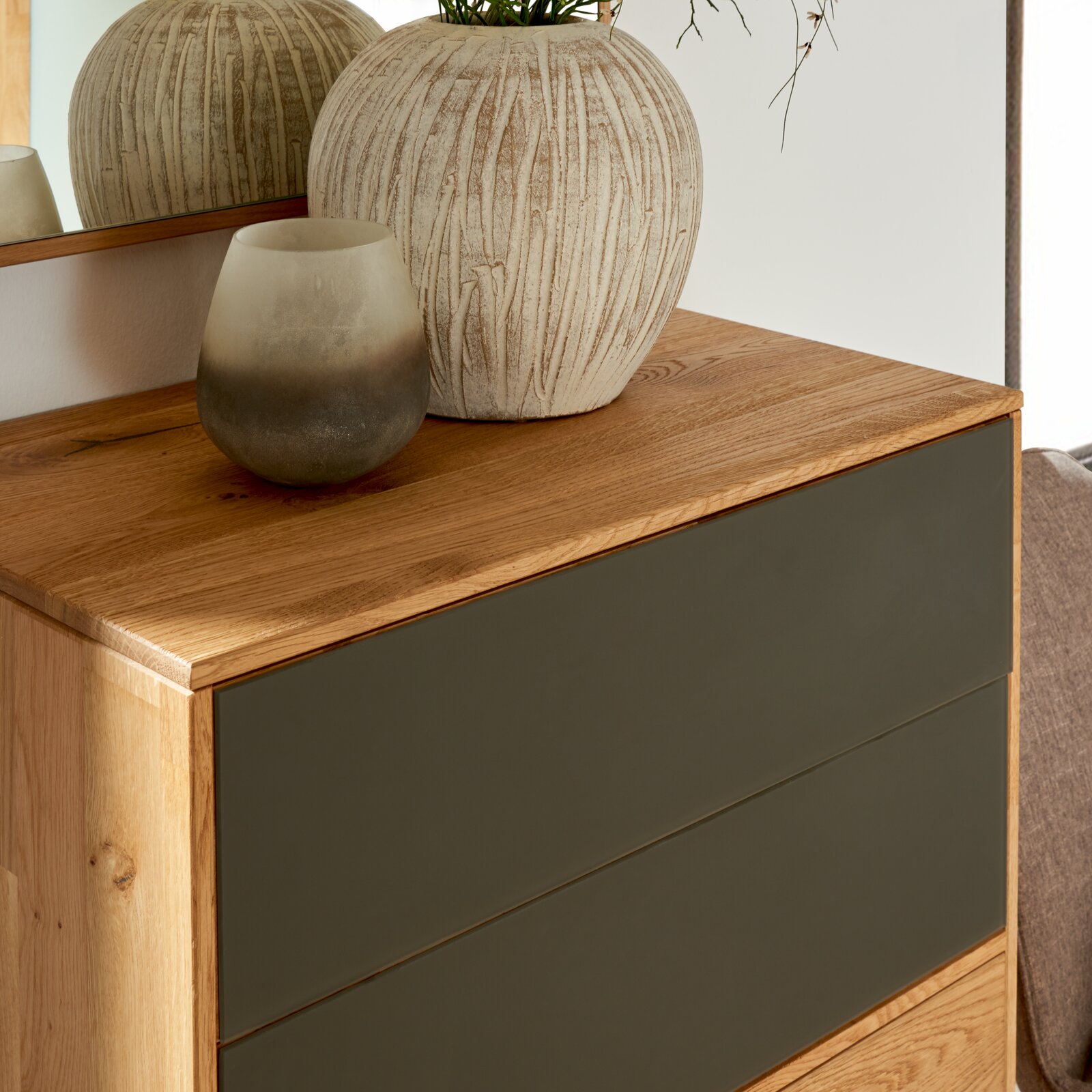 Nahaufnahme eines modernen Schuhschranks aus Holz mit dunklen Schubladenfronten, dekoriert mit einer großen, strukturierten Vase und einem kleinen, getönten Glasgefäß auf der Oberseite.