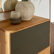 Nahaufnahme eines modernen Schuhschranks aus Holz mit dunklen Schubladenfronten, dekoriert mit einer großen, strukturierten Vase und einem kleinen, getönten Glasgefäß auf der Oberseite.