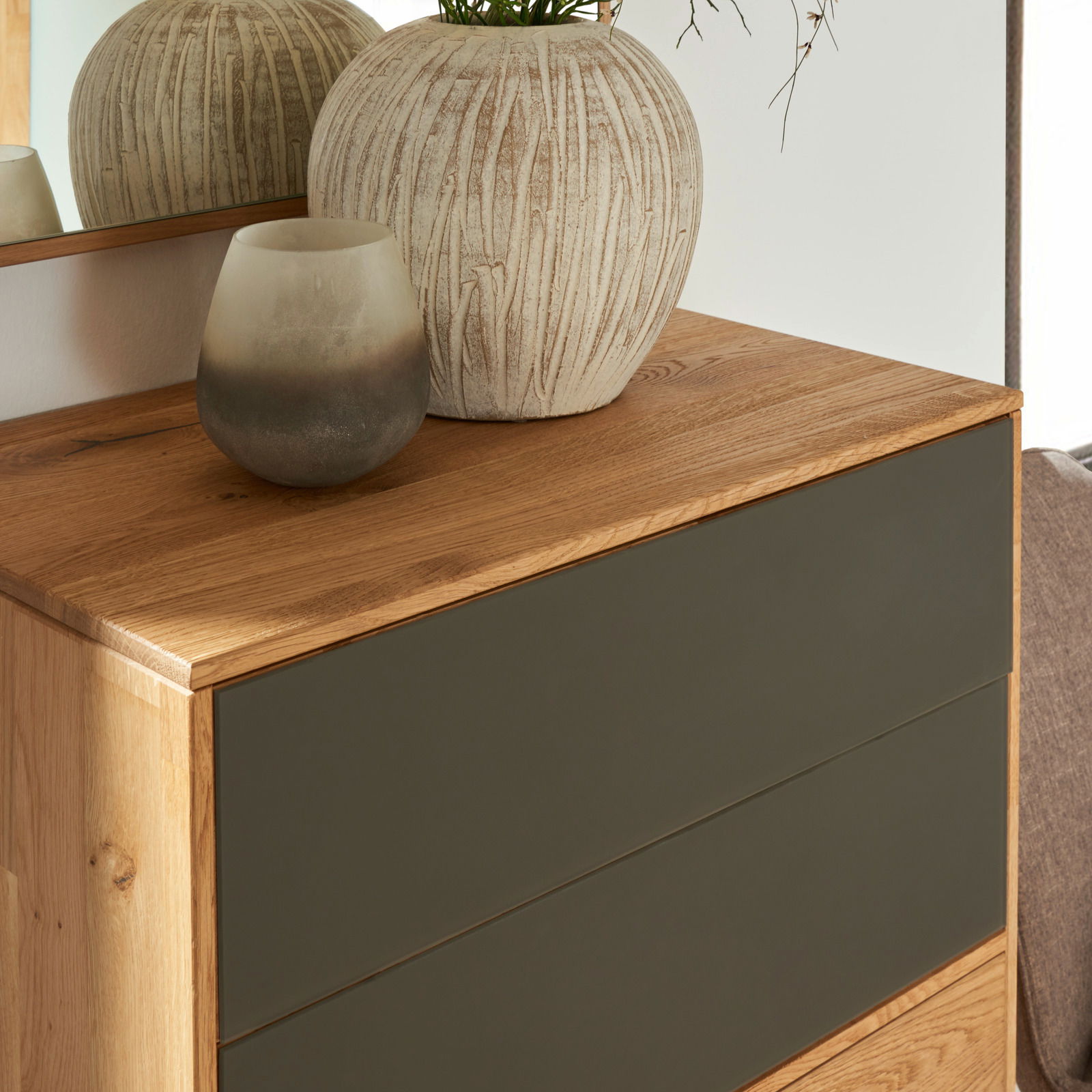 Nahaufnahme eines modernen Schuhschranks aus Holz mit dunklen Schubladenfronten, dekoriert mit einer großen, strukturierten Vase und einem kleinen, getönten Glasgefäß auf der Oberseite.