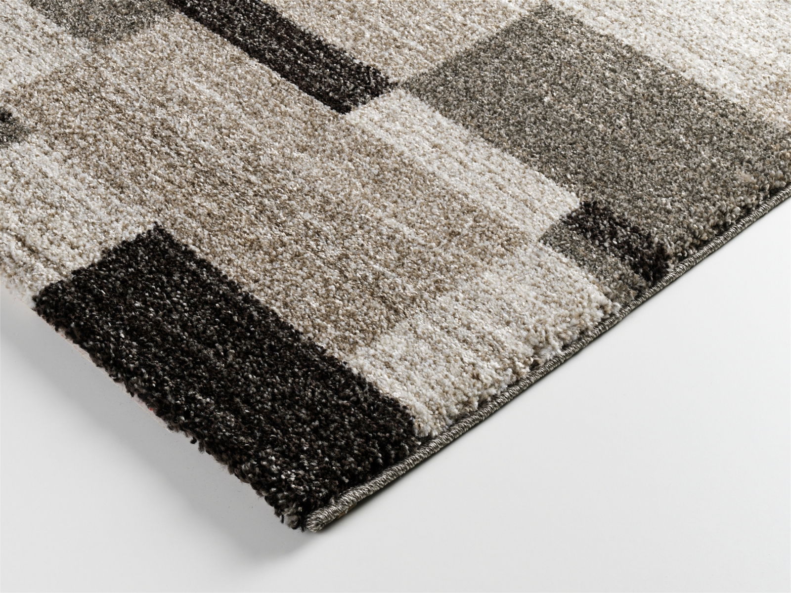 Nahaufnahme eines rechteckigen Teppichs mit einem modernen, geometrischen Muster in verschiedenen Grautönen. Perspektive von der Seite.