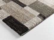 Nahaufnahme eines rechteckigen Teppichs mit einem modernen, geometrischen Muster in verschiedenen Grautönen. Perspektive von der Seite.