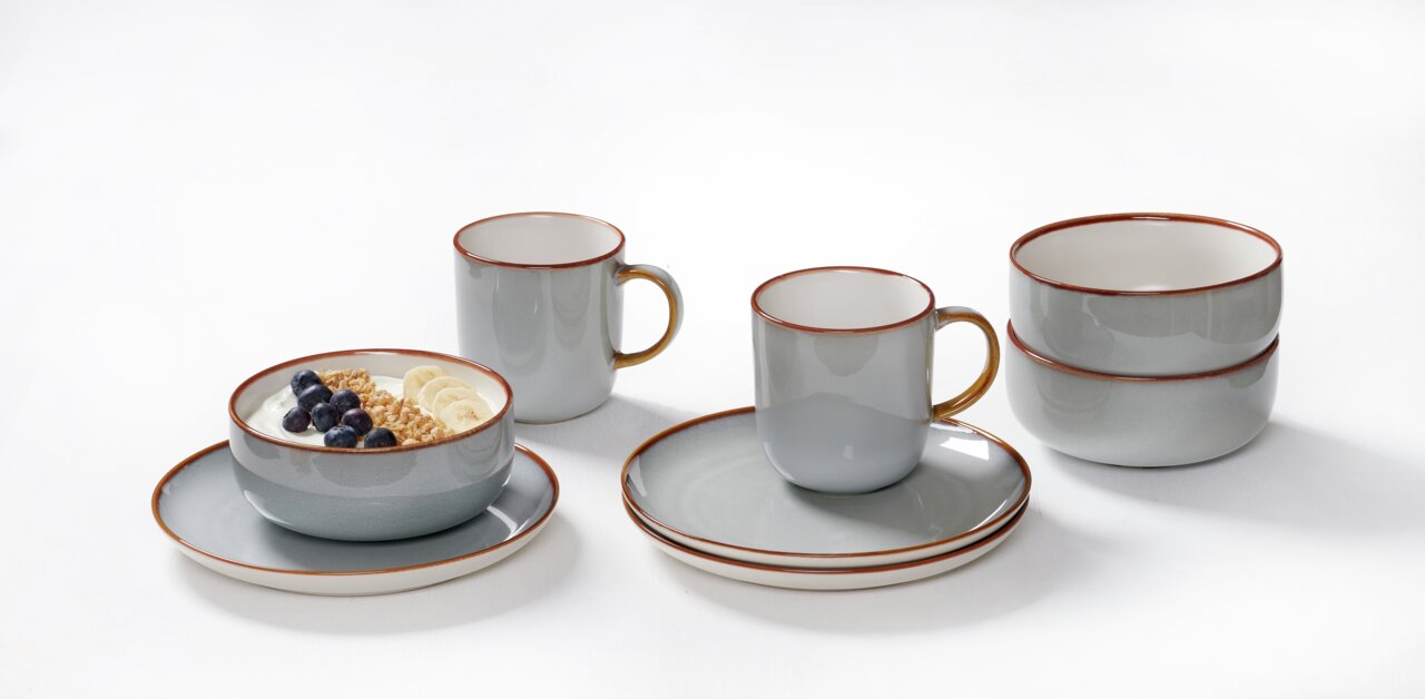 Ritzenhoff & Breker Frühstücksset 12-tlg. PORTOFINO Frühstücksset Portofino 12-tlg in grauer Keramik mit braunem Rand, bestehend aus Tassen, Schalen und Tellern, auf weißem Hintergrund aus seitlicher Perspektive.