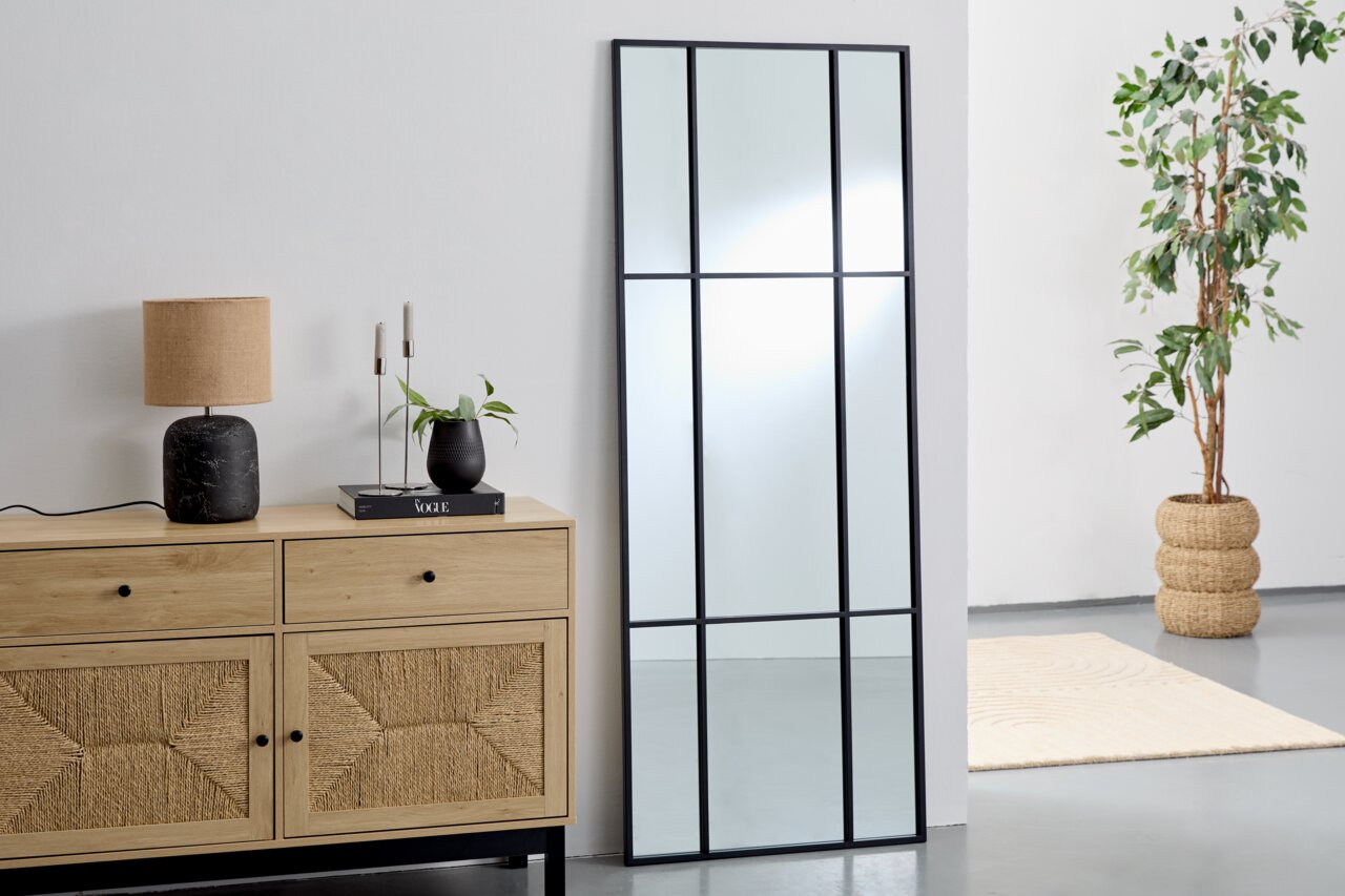 Landscape Spiegel ARON Großer rechteckiger Spiegel mit schwarzem Rahmen, an eine weiße Wand gelehnt, neben einer Holzkommode mit Dekorationen, aus seitlicher Perspektive.