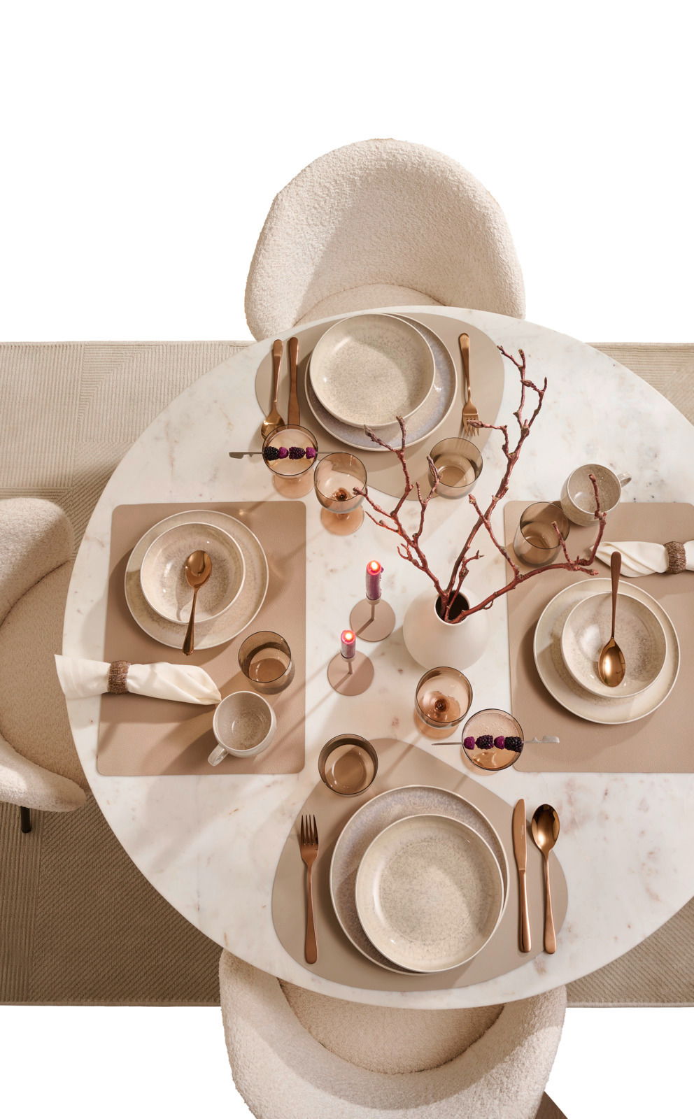 Elegantes Tafelservice für vier Personen auf einem runden Marmortisch, aus der Vogelperspektive fotografiert. Enthält Teller, Schalen, Besteck und Gläser in warmen Erdtönen, dekoriert mit Kerzen und Zweigen.