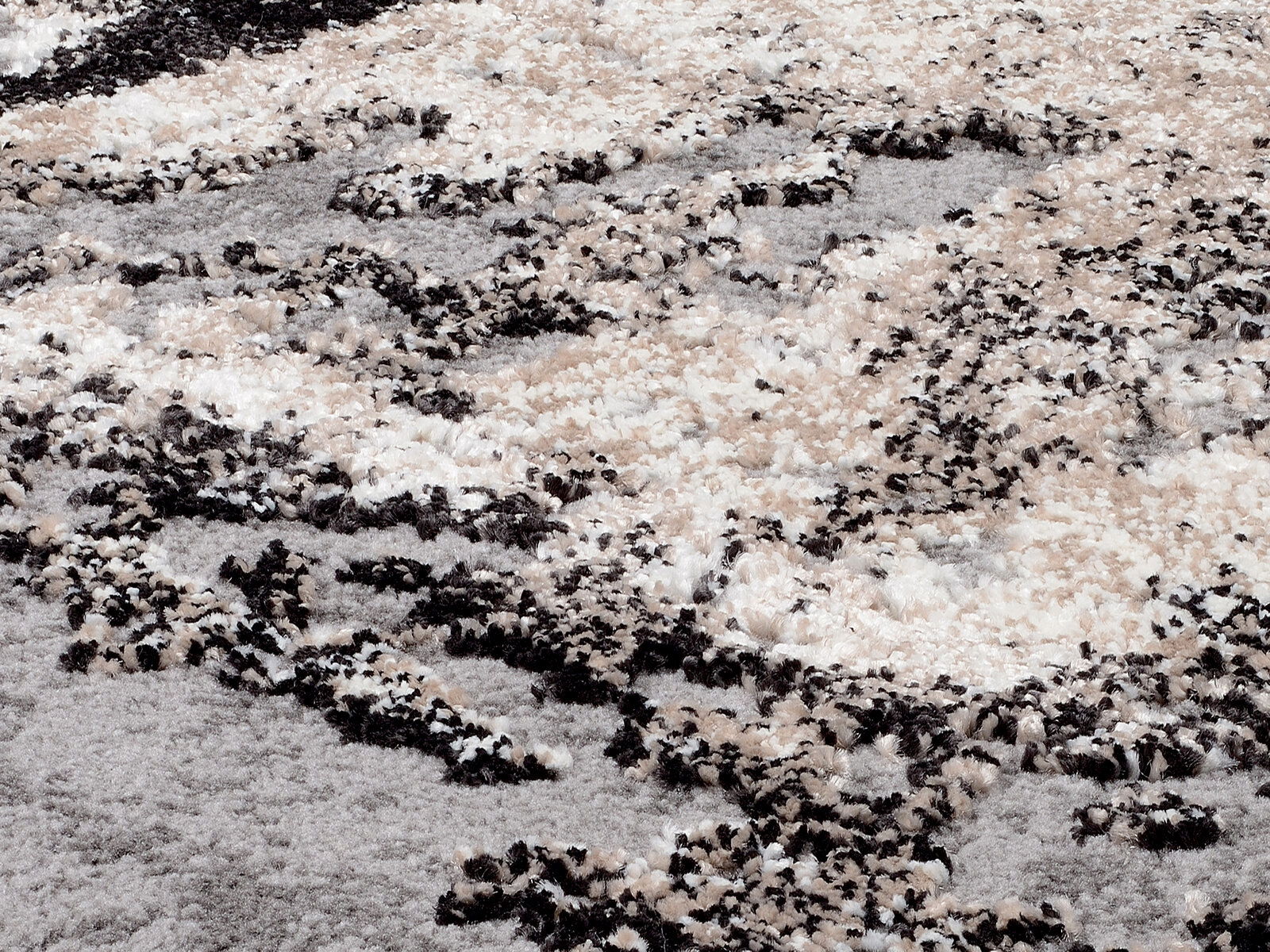 Nahaufnahme eines flauschigen Teppichs mit abstraktem Muster in Beige-, Grau- und Schwarztönen, aus seitlicher Perspektive aufgenommen.