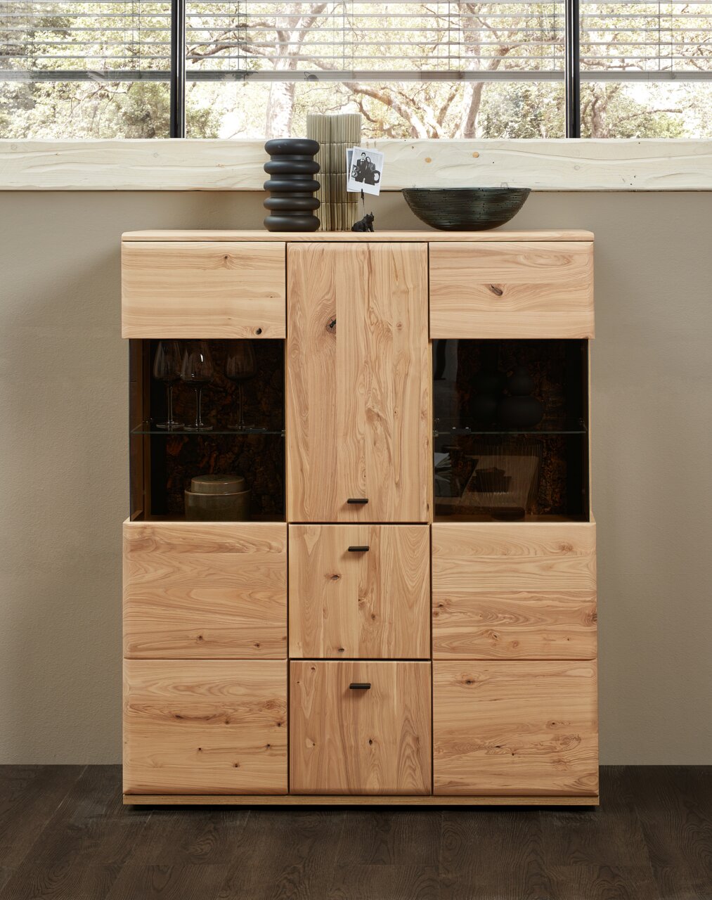 Cantus Highboard CALMERA Frontale Ansicht eines Highboards aus Holz mit mehreren Schubladen und Türen, dekoriert mit Vasen und einer Schale auf der Oberseite.