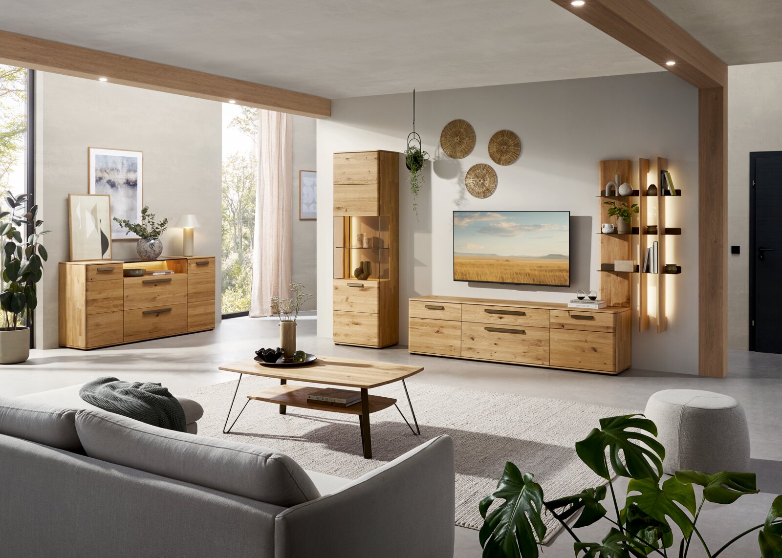 Modernes Wohnzimmer-Set aus massiver Eiche mit Sideboard, Vitrine und TV-Lowboard samt Wandregal und Couchtisch, fotografiert in leichter Weitwinkel-Frontansicht aus Augenhöhe.