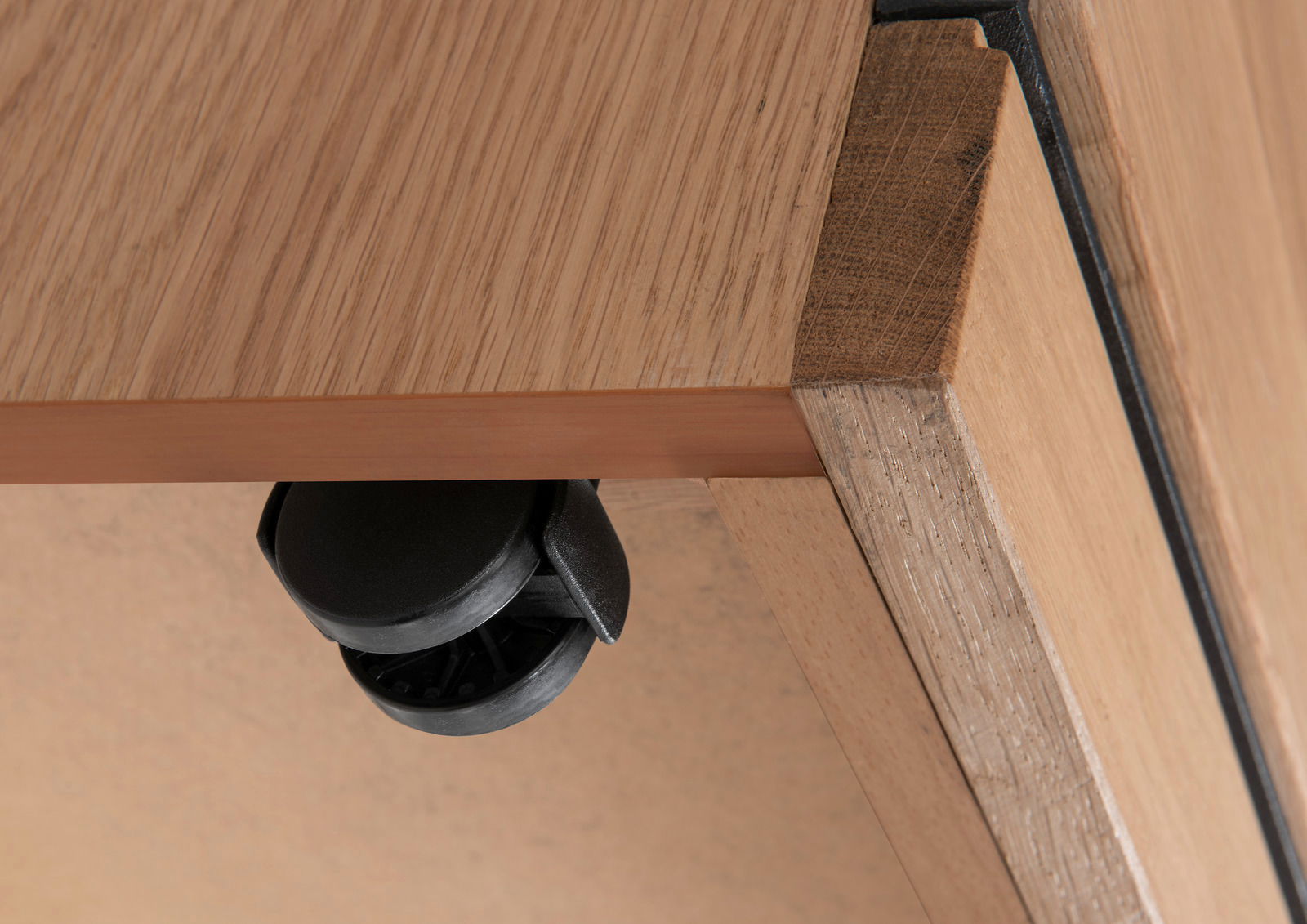Nahaufnahme einer Roll-Kommode aus Holz mit schwarzem Rad, von unten betrachtet.