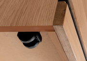 Nahaufnahme einer Roll-Kommode aus Holz mit schwarzem Rad, von unten betrachtet.