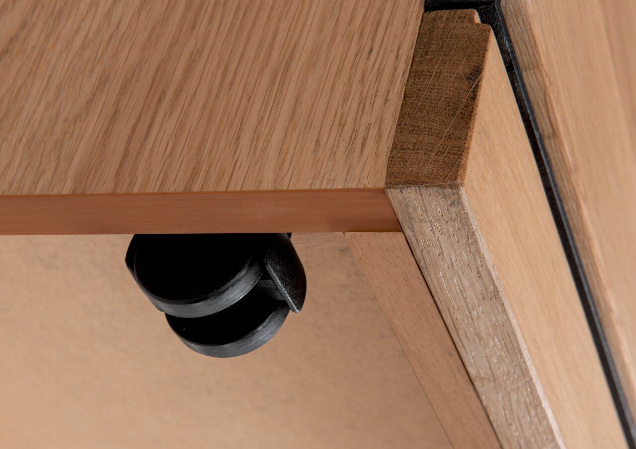 Nahaufnahme einer Roll-Kommode aus Holz mit schwarzem Rad, von unten betrachtet.