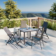 Moderner Gartentisch auf einer Terrasse mit Blick auf die Berge, umgeben von vier Stühlen und dekoriert mit Geschirr und einer Vase. Perspektive von schräg oben.