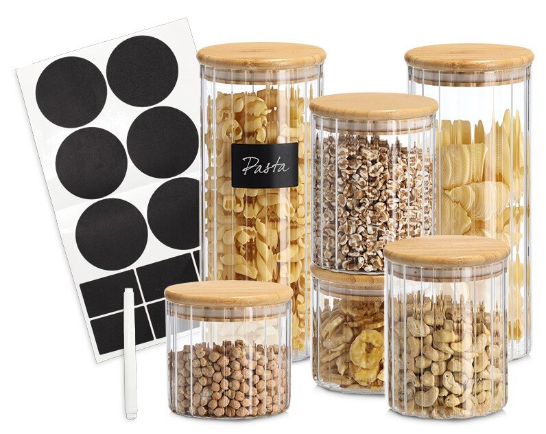 Zeller Present Set van 6 ronde voorraadpotten Een set van zes doorzichtige voorraadpotten met bamboedeksels, gefotografeerd vanuit een schuine hoek van voren, gevuld met pasta, muesli, noten en peulvruchten, met daarnaast zwarte etikettenstickers en een wit krijtstiftje.