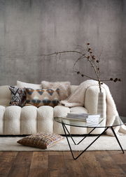 Gemütliches Wohnzimmer mit modernem Sofa, dekoriert mit verschiedenen Kissenhüllen in Erdtönen und geometrischen Mustern, aus der Perspektive von vorne.