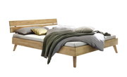 Holzbett mit modernem Kopfteil aus Holz und Metall, seitliche Perspektive, dekoriert mit Kissen und Decke.
