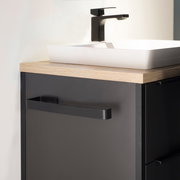 Moderner schwarzer Handtuchhalter an einem dunklen Badezimmerschrank, seitliche Perspektive.