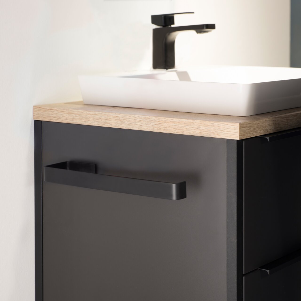 Moderner schwarzer Handtuchhalter an einem dunklen Badezimmerschrank, seitliche Perspektive.