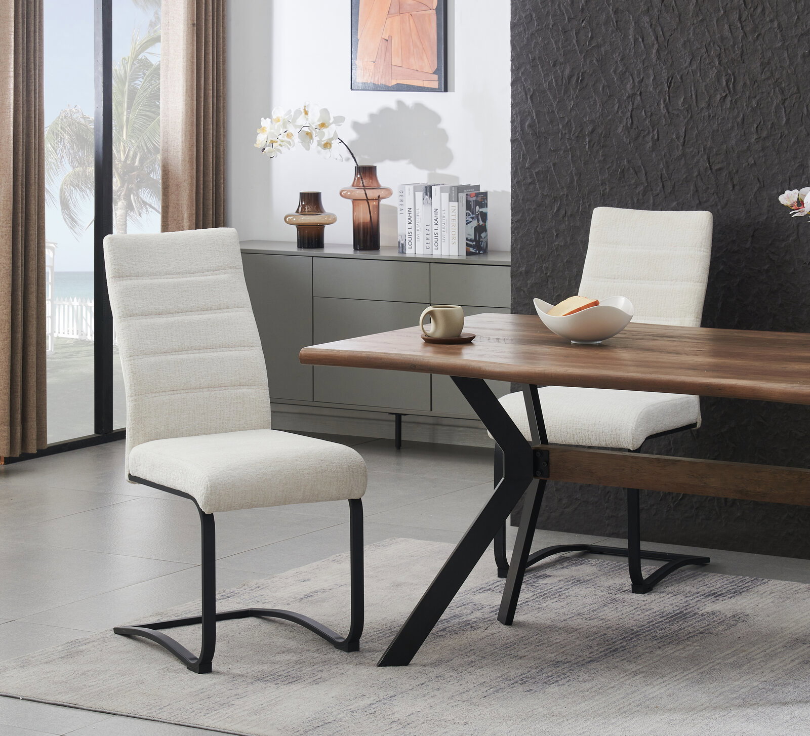 Moderner Freischwinger-Esszimmerstuhl mit hellbeigem Stoffbezug und schwarzem Metallgestell, seitliche Perspektive im Wohn-/Essbereich neben Holzesstisch.