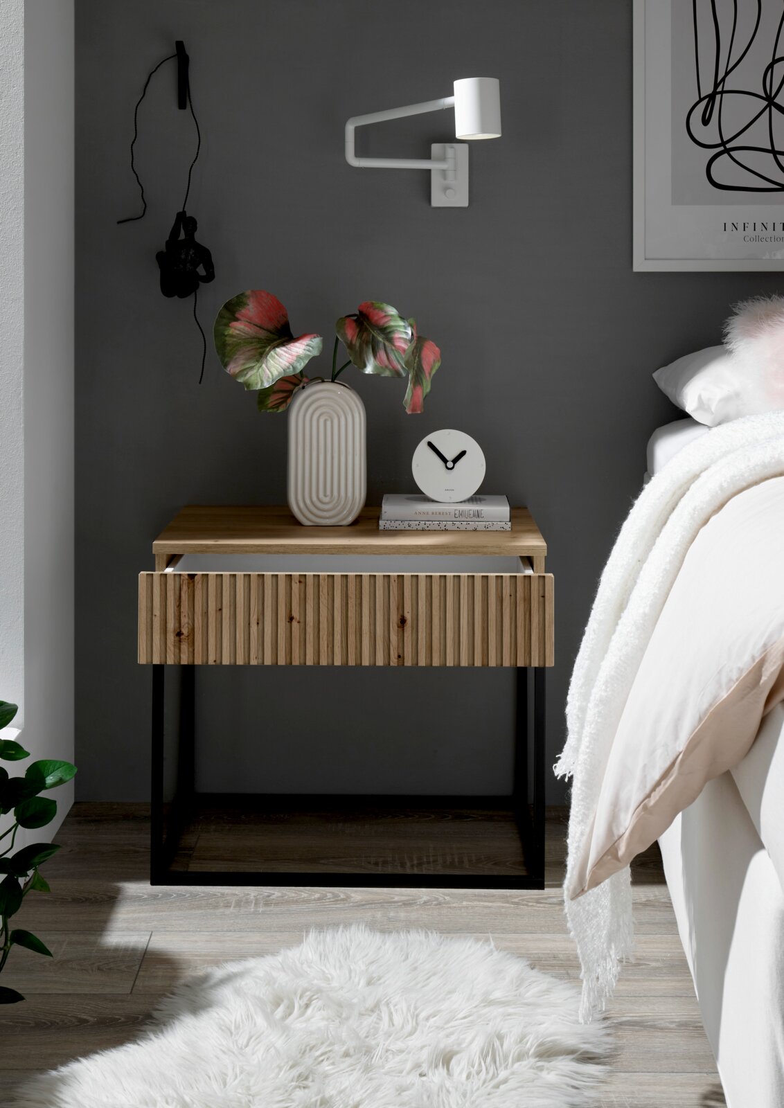Moderne Nachtkommode mit Holzfront und schwarzem Metallrahmen, dekoriert mit einer Vase und einer Uhr, seitliche Perspektive.