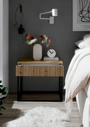 Moderne Nachtkommode mit Holzfront und schwarzem Metallrahmen, dekoriert mit einer Vase und einer Uhr, seitliche Perspektive.