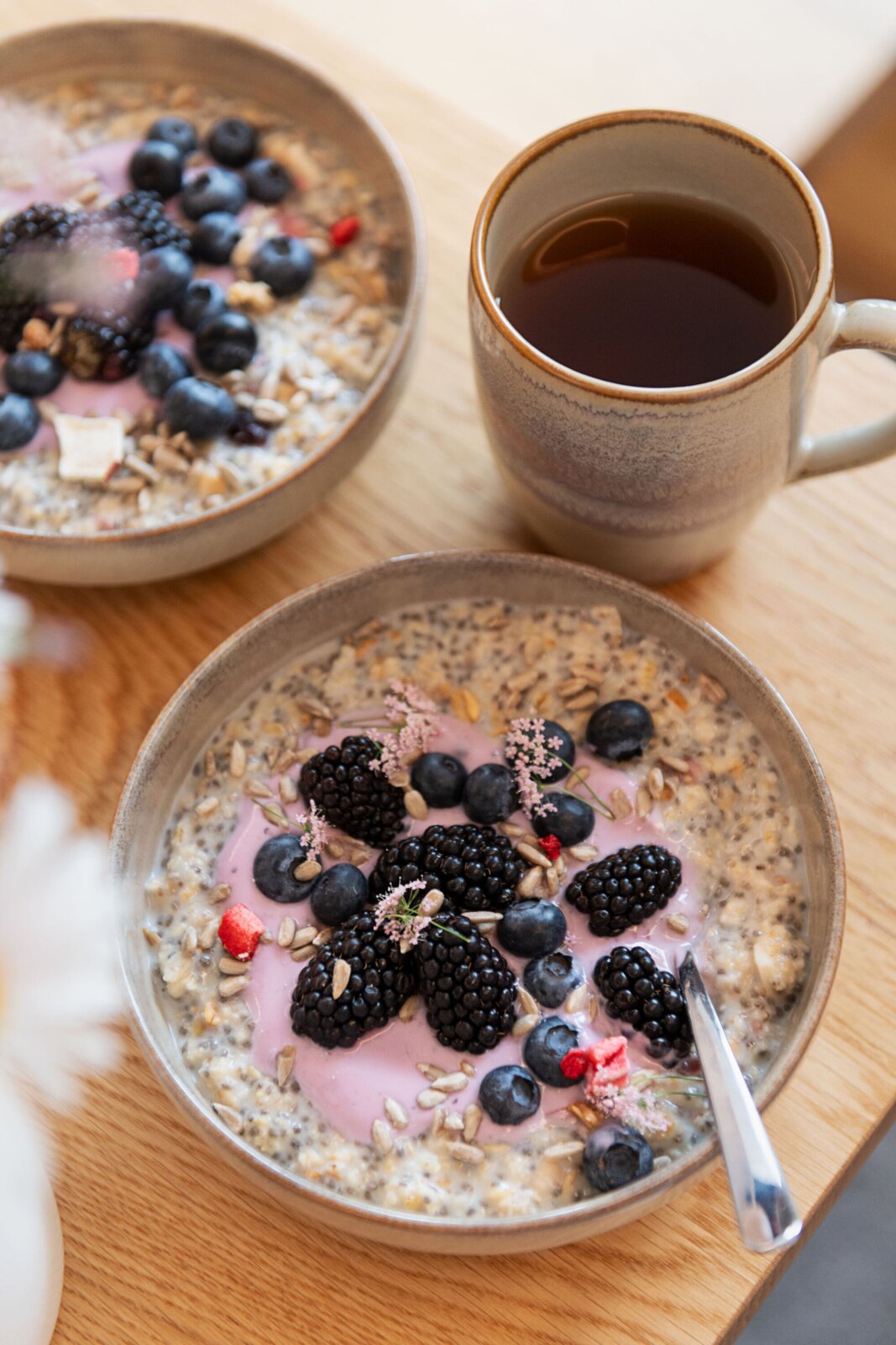 Gipfelstück Kaffeebecher 4er-Set NEBELWALD Schalen mit cremigem Porridge/Müsli, getoppt mit Joghurt, Blaubeeren, Brombeeren und Saaten, daneben eine Tasse Tee auf Holzbrett; Perspektive: leicht von oben (Top-Down/Schrägansicht).