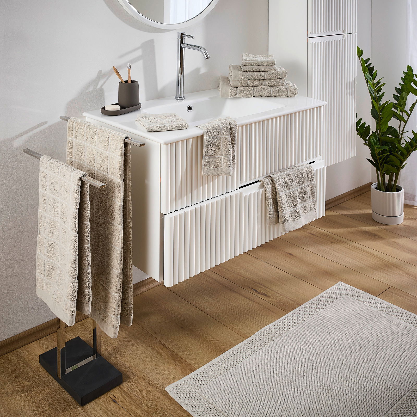 Badezimmer mit Frottierset in Beige, bestehend aus Handtüchern und Waschlappen, auf einem weißen Waschtisch arrangiert. Perspektive von schräg oben.