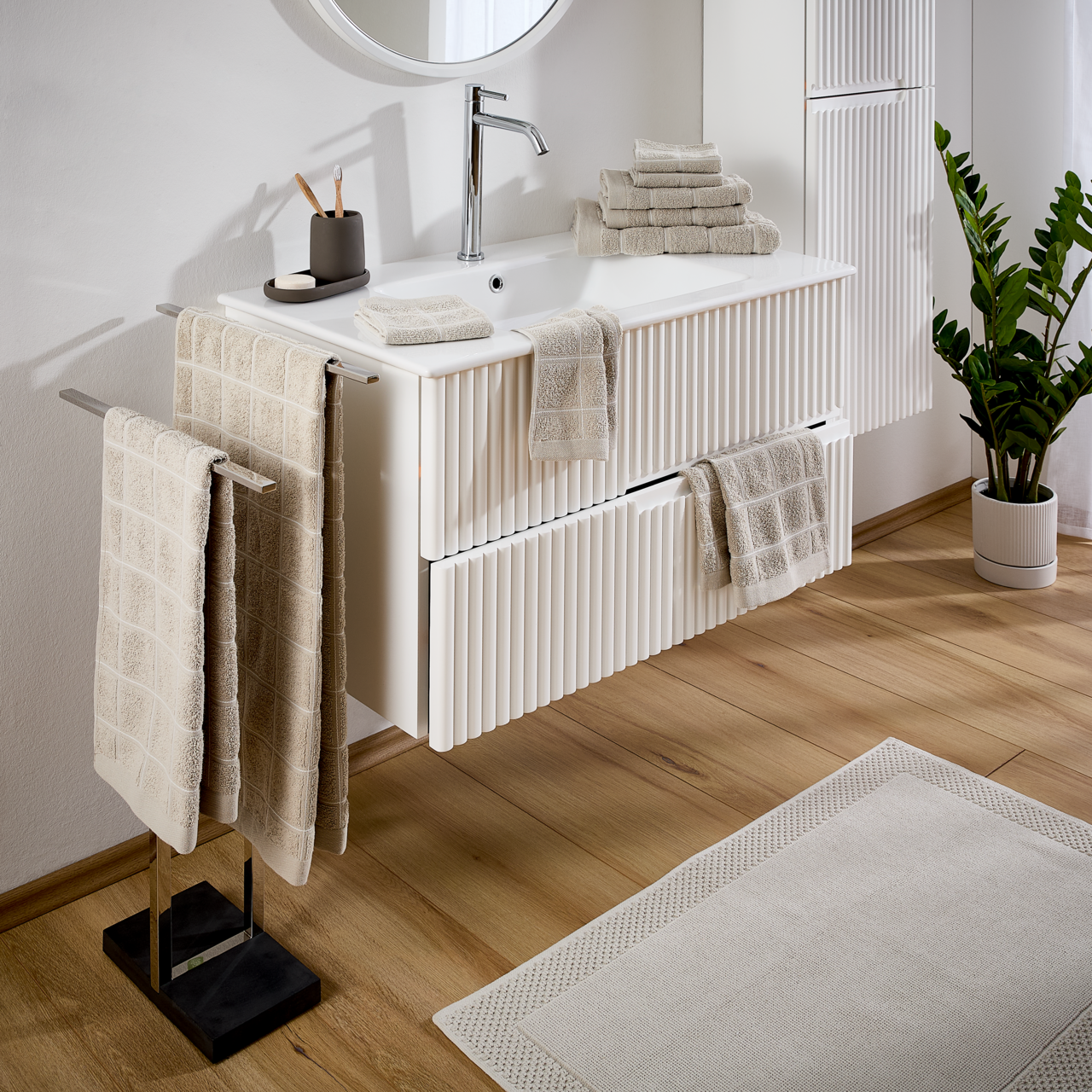 Badezimmer mit Frottierset in Beige, bestehend aus Handtüchern und Waschlappen, auf einem weißen Waschtisch arrangiert. Perspektive von schräg oben.