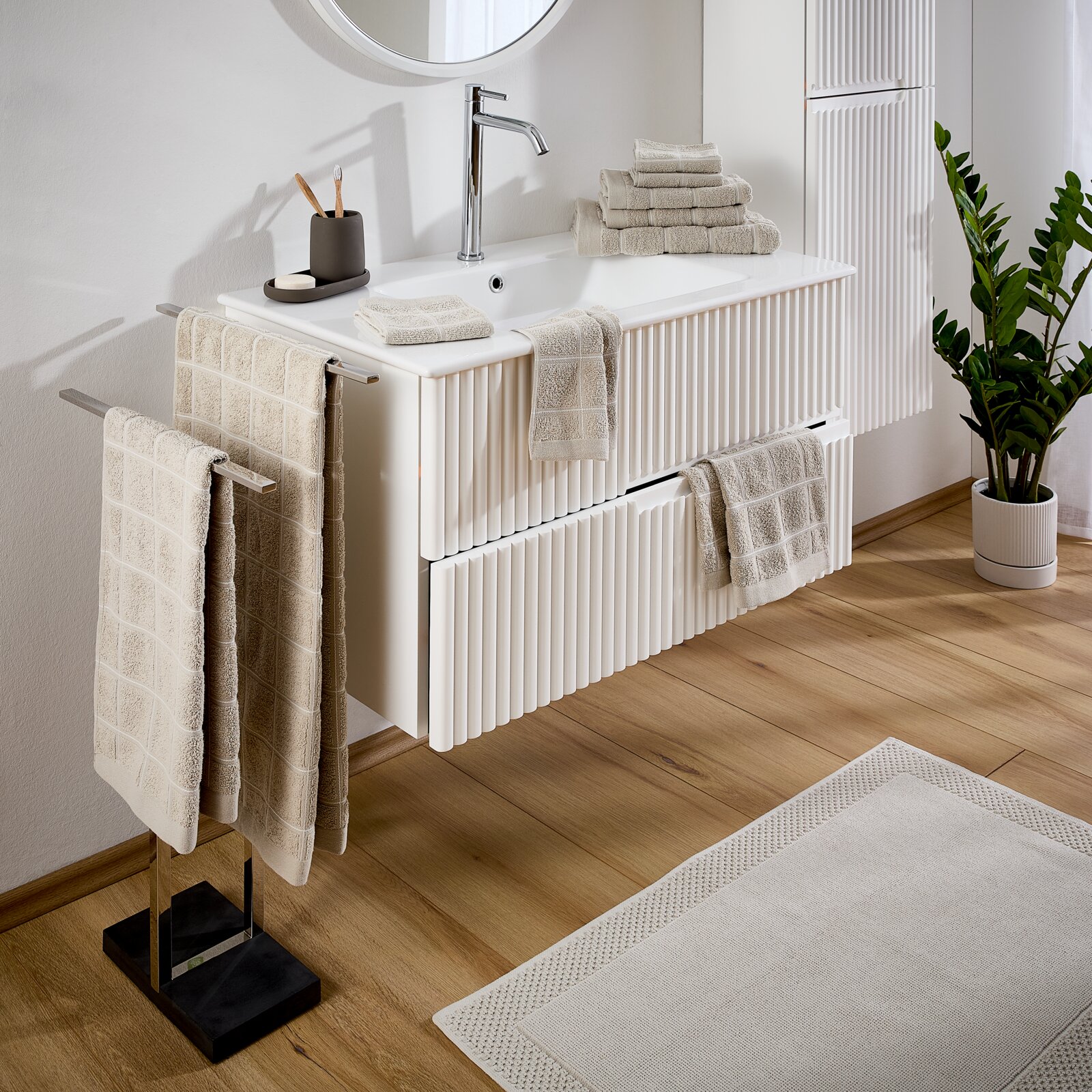 Esposa Badstofset Badkamer met een set badhanddoeken in beige, bestaande uit handdoeken en washandjes, neergelegd op een witte wastafel. Aanzicht van schuin bovenaf.
