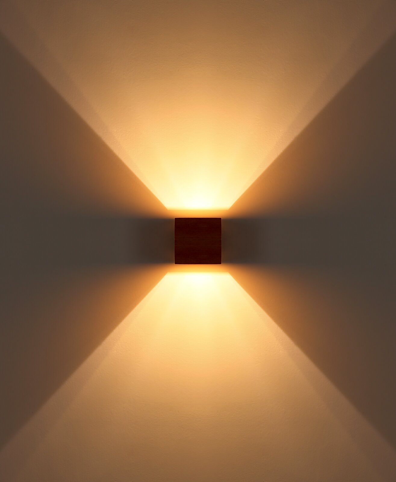 Moderne quadratische Wandleuchte in dunkler Holzoptik mit warmweißem Up-and-Down-Light, frontale Ansicht an heller Wand mit symmetrischem Lichtkegel nach oben und unten