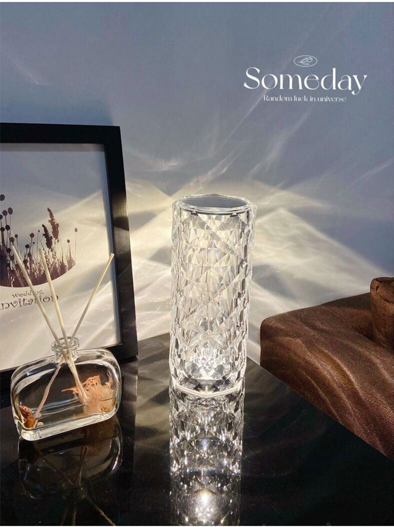 LED-Dekoleuchte in zylindrischer Form mit facettiertem Glasdesign, auf einem Tisch neben einem Bilderrahmen und einem Duftdiffusor, seitliche Perspektive.