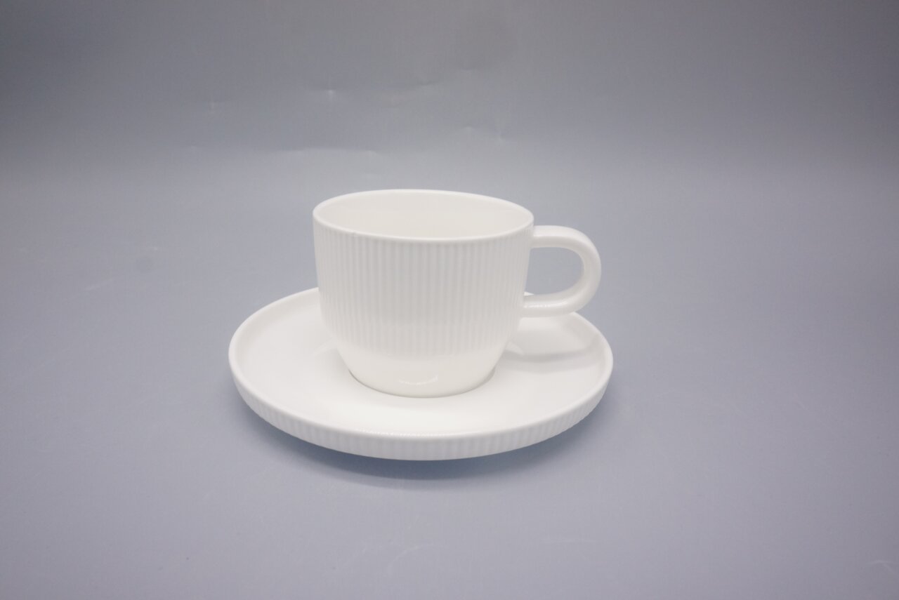 Zurbrüggen Cappuccinotasse 4-tlg. Weiße Porzellan-Kaffeetasse mit Untertasse und feiner Rillenstruktur, in schräger Vorderansicht mit Henkel rechts auf neutralgrauem Hintergrund