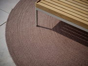 Runder Outdoor-Teppich in einem warmen Braunton, teilweise unter einer Holzbank, aus der Vogelperspektive fotografiert.