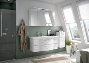 Moderne Badezimmeransicht mit weißem Badblock, bestehend aus einem Waschbecken mit Unterschrank und einem Spiegelschrank, seitlich ein hoher Schrank, alles in einer hellen, lichtdurchfluteten Umgebung mit schrägen Fenstern.