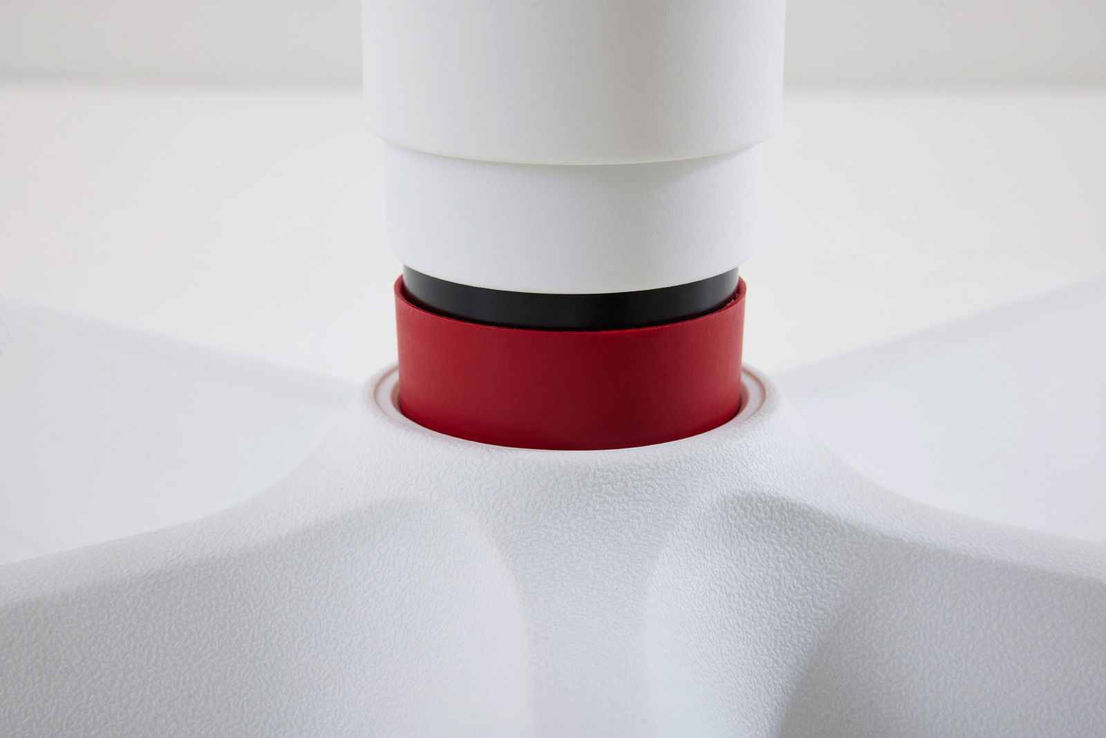 Nahaufnahme eines Jugenddrehstuhls mit weißer und roter Farbgebung, Fokus auf die Verbindung zwischen Sitz und Basis.