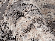 Nahaufnahme eines Designer Teppichs mit abstraktem Muster in Grau-, Beige- und Schwarztönen, perspektivisch von der Seite aufgenommen.