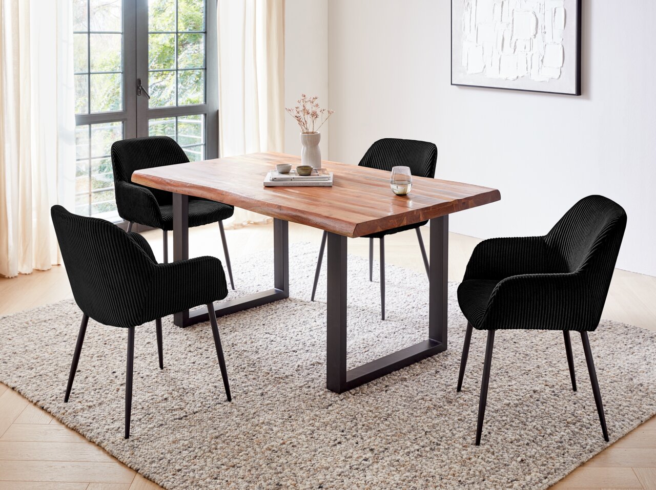 Esszimmer mit einem Holztisch und vier schwarzen Armlehnstühlen aus Stoff, Perspektive von schräg oben.