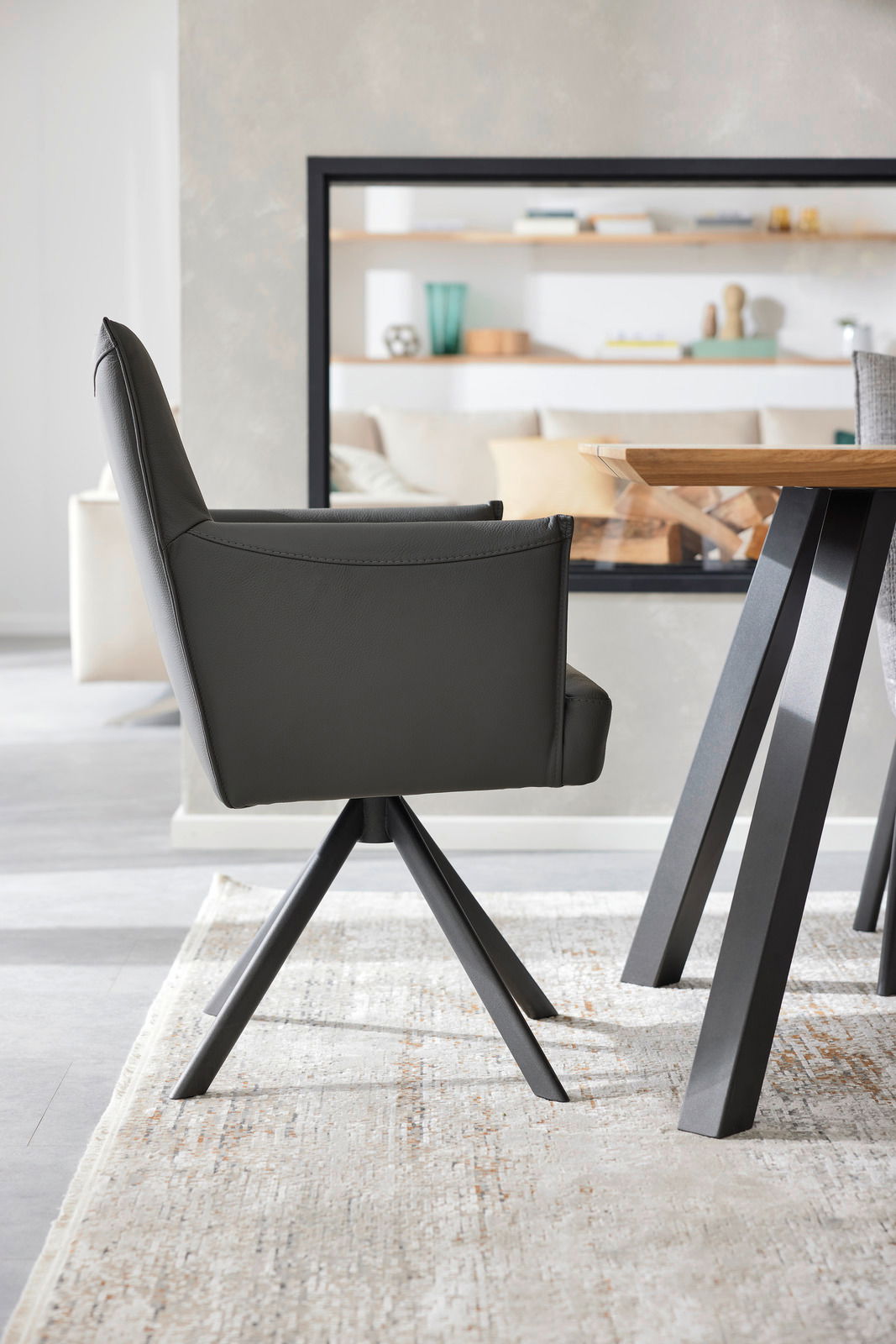 Seitenansicht eines modernen Armlehnstuhls mit schwarzem Lederbezug und Metallbeinen, neben einem Holztisch in einem stilvollen Wohnzimmer.