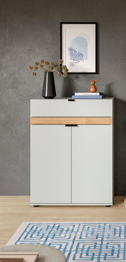 Modernes Sideboard in Hellgrau mit Holz-Akzentleiste und zwei Türen vor grauer Wand, dekoriert mit Vase, Büchern und Holzvogel; Frontalansicht auf Augenhöhe.