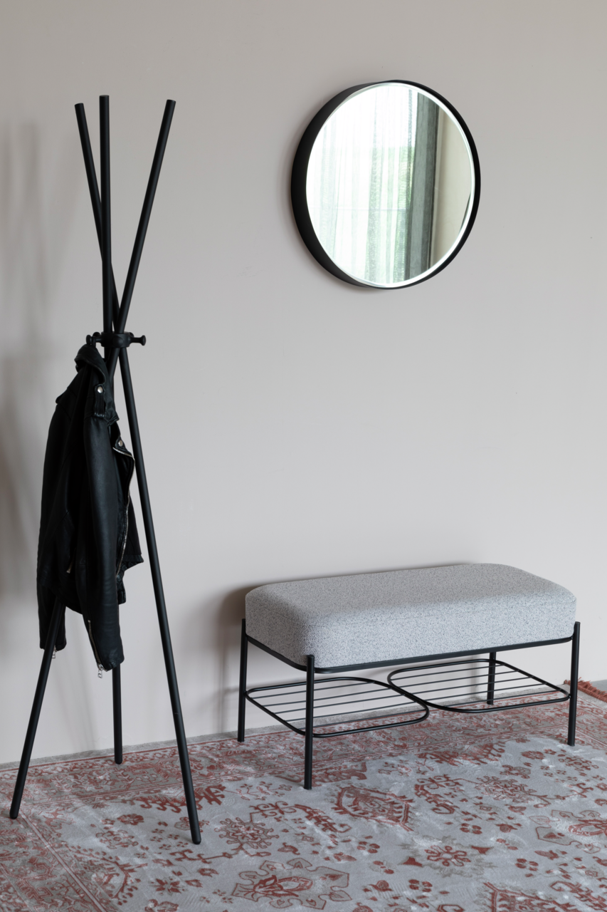 Moderne Sitzbank mit grauem Polster und schwarzem Metallgestell, seitliche Perspektive, neben einem Kleiderständer und einem runden Spiegel an der Wand.
