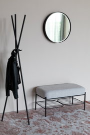 Moderne bank met grijze bekleding en een zwart metalen frame, gezien vanaf de zijkant, naast een kledingrek en een ronde spiegel aan de muur.