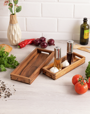 Längliches Servier-Tablett aus Holz, von oben fotografiert, umgeben von frischen Zutaten wie Tomaten, Paprika und Kräutern.