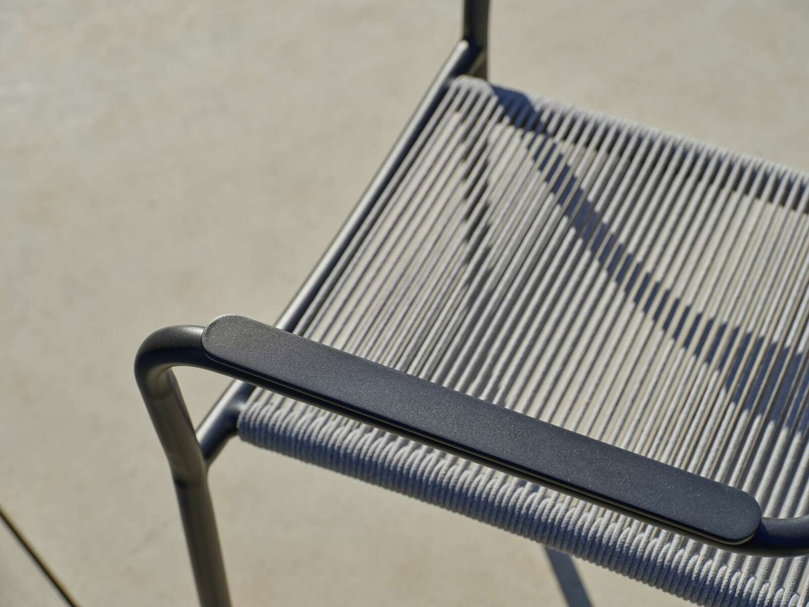 Nahaufnahme eines Stapelsessels mit Metallrahmen und geflochtener Sitzfläche, von oben betrachtet.