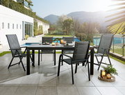 Moderner Gartentisch mit vier Stühlen auf einer Terrasse, umgeben von grüner Landschaft und Pool, aus seitlicher Perspektive fotografiert.