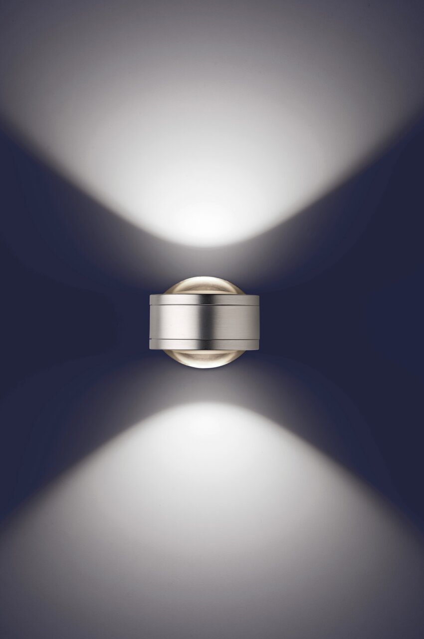 Moderne LED Wandleuchte in silberner Optik, die von oben betrachtet wird und ein elegantes Lichtmuster an die Wand projiziert.