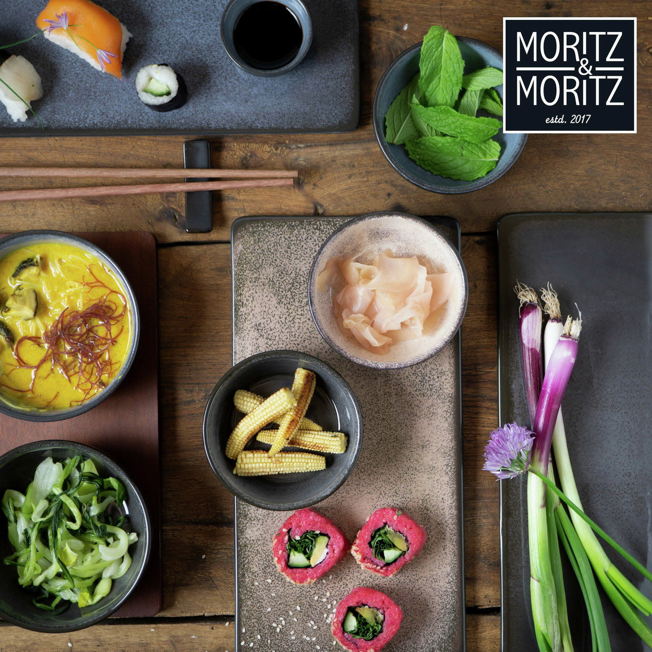 Vogelperspektive auf ein stilvolles Sushi-Set mit blauen Tellern, Sushi, Sojasauce, Ingwer, Minze, Babymais und Frühlingszwiebeln.