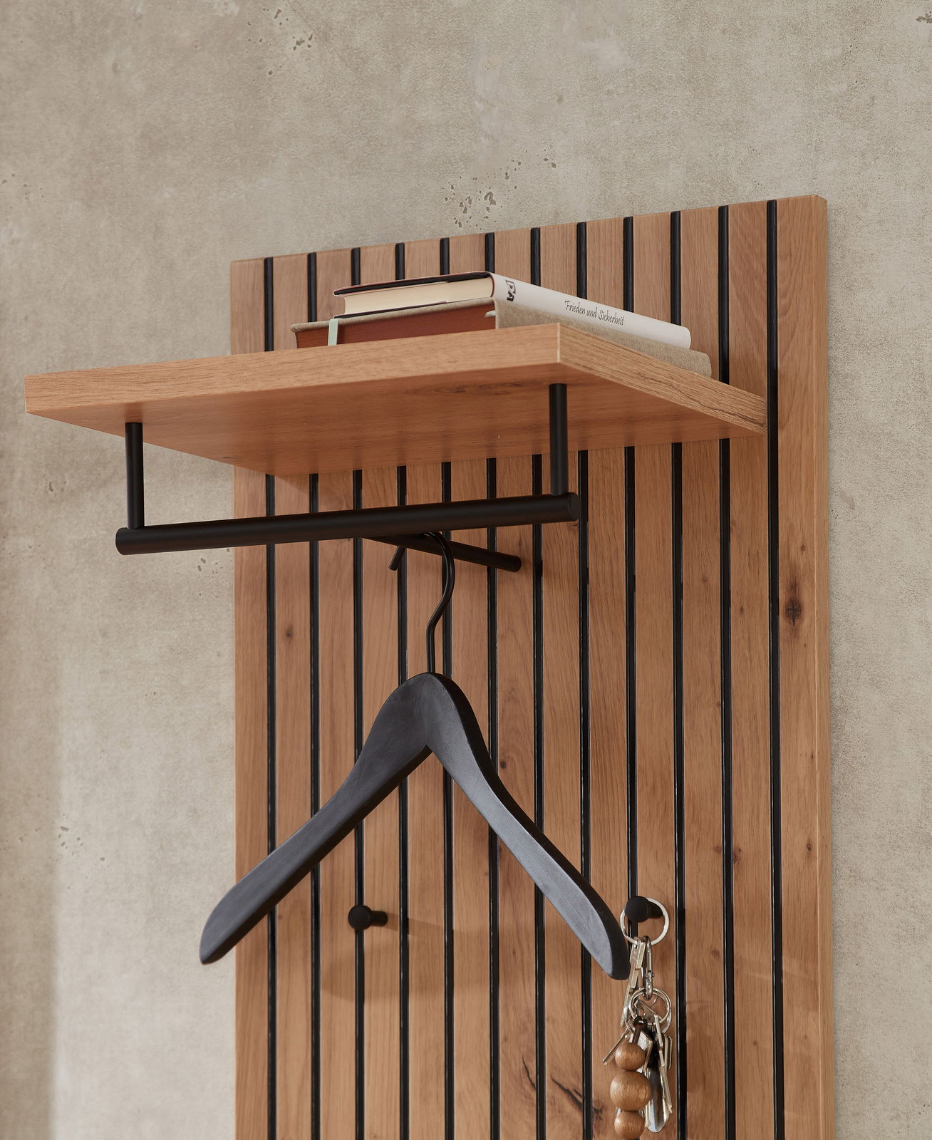 Nahaufnahme eines modernen Garderobenpaneels aus Holz mit schwarzem Kleiderbügel und Ablage für Bücher.