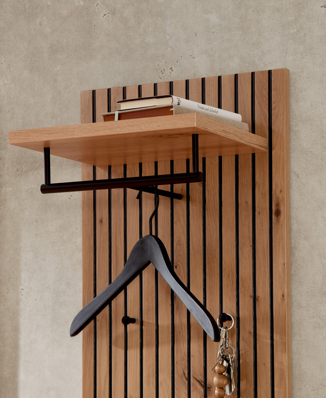 Nahaufnahme eines modernen Garderobenpaneels aus Holz mit schwarzem Kleiderbügel und Ablage für Bücher.