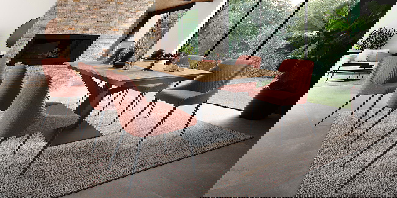 Ein stilvolles Esszimmer mit Holztisch, rosa Stühlen, Kamin und großer Fensterfront mit Gartenblick.