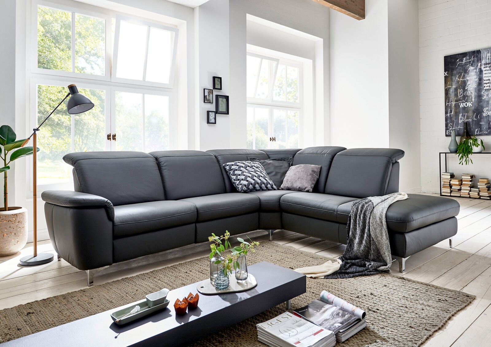 Moderne graue Leder-Eckcouch mit Ottomane und Metallfüßen im hellen Wohnzimmer, Frontansicht in leichter Schrägperspektive von links