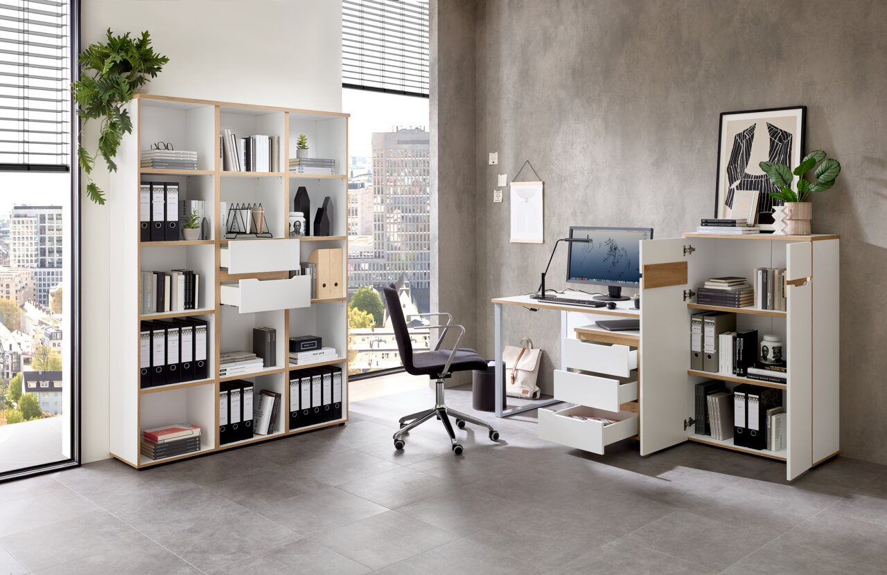 Moderne Büroumgebung mit Regalsystem, Schreibtisch und Rollcontainer in heller Holzoptik, seitliche Perspektive.