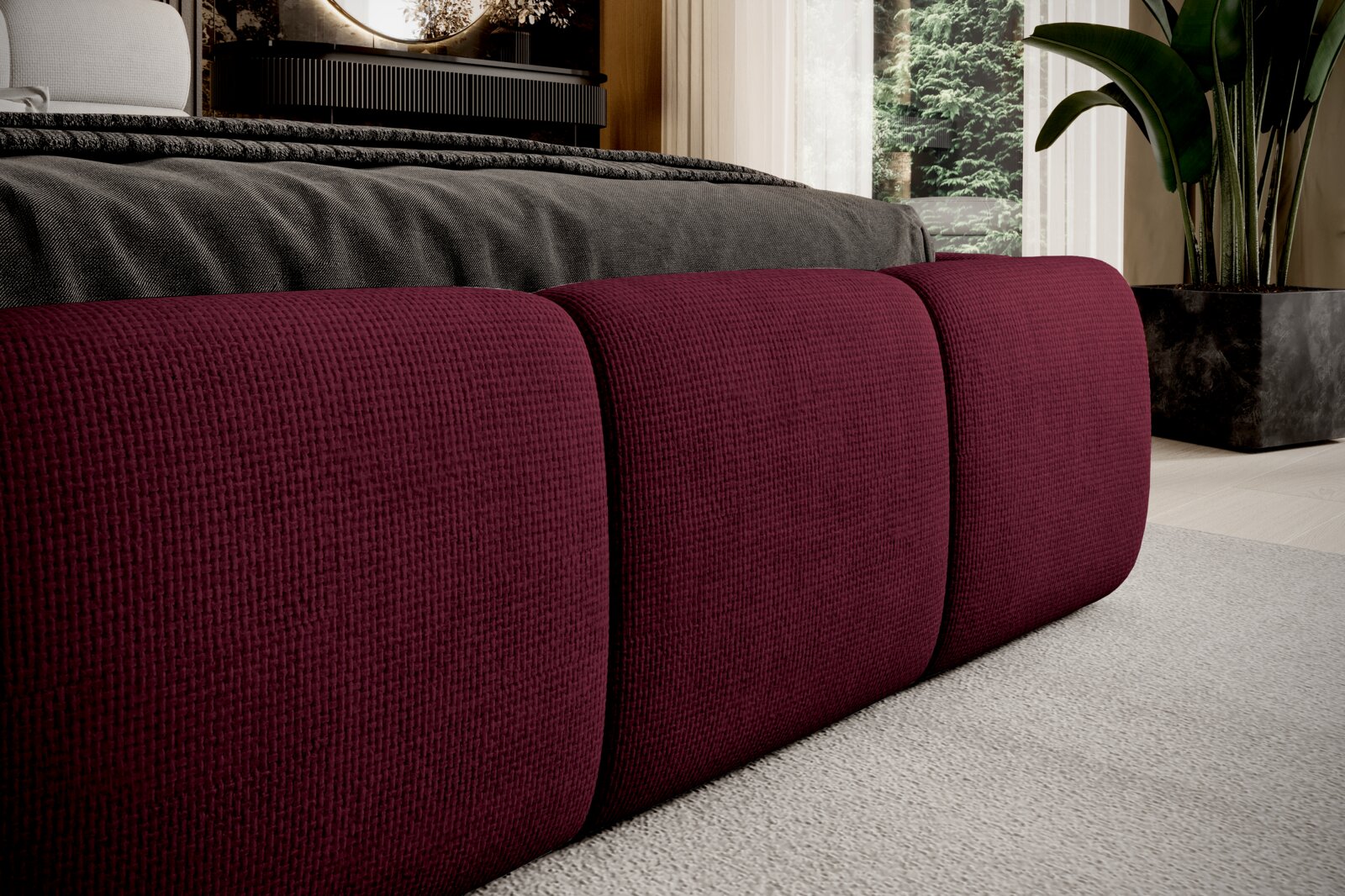 Close-up van een gestoffeerd bed met een wijnrode bekleding, gezien vanaf de zijkant